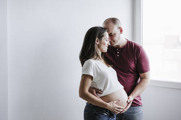 Pregnant woman standing with man touching belly at home - EBBF05668