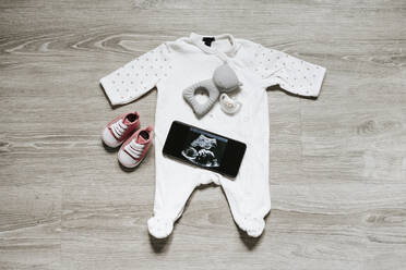Babykleidung und Schnuller mit Ultraschallbild auf dem Smartphone zu Hause - EBBF05673