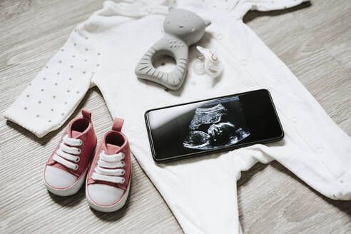 Babyschühchen mit Schnuller und Ultraschallbild auf dem Smartphone zu Hause - EBBF05674