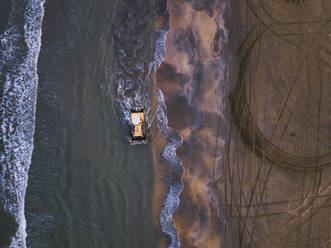 Russia, Dagestan, Derbent, Aerial view of bulldozer driving along sandy seashore - KNTF06570