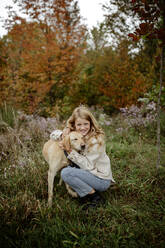 Lächelndes blondes Mädchen, das seinen Hund im Garten umarmt - ELEF00001