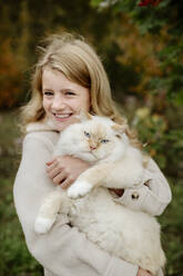 Glückliches blondes Mädchen mit Ragdoll-Katze im Garten - ELEF00002