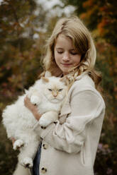 Blondes Mädchen mit Ragdoll-Katze im Garten - ELEF00004