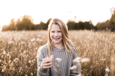 Glückliches blondes Mädchen hält Blume auf Feld bei Sonnenuntergang - ANF00004