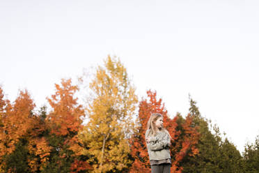 Blond girl with arms crossed in front of autumn trees at park - ANF00006