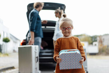 Girl holding suitcase with parents loading luggage in car - JOSEF07044