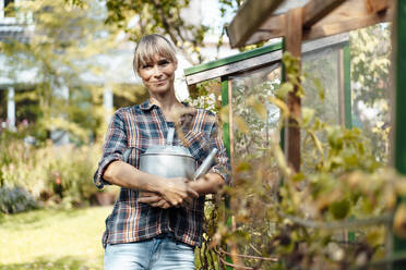 Smiling woman with watering can standing in garden - JOSEF07052