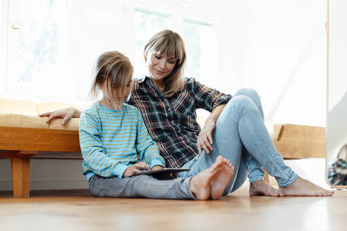 Mutter betrachtet ihren Sohn bei der Nutzung eines digitalen Tablets auf dem Boden zu Hause - JOSEF07084