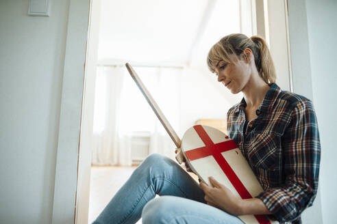 Woman sitting with wooden sword and shield at home - JOSEF07095