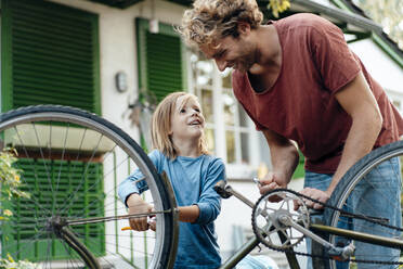 Smiling father and son repairing bicycle in back yard - JOSEF07130