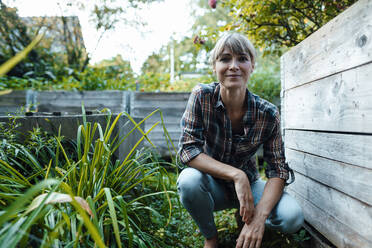 Woman kneeling by plants in back yard - JOSEF07160