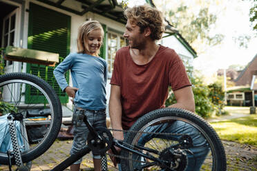 Smiling father and son repairing bicycle outside house - JOSEF07163