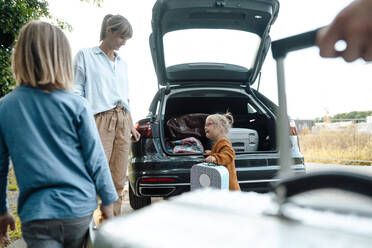 Mother looking at daughter with suitcase by car trunk on vacation - JOSEF07168