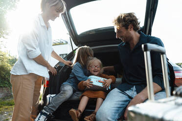 Parents looking at son embracing daughter in car trunk - JOSEF07170