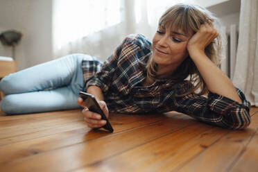 Woman with bangs using smart phone on floor at home - JOSEF07177