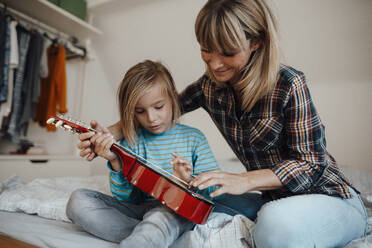 Mother teaching son to play guitar in bedroom at home - JOSEF07179