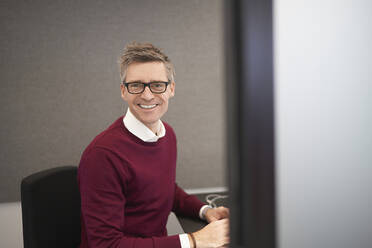 Lächelnder Geschäftsmann sitzt auf einem Stuhl im Büro - JAHF00095