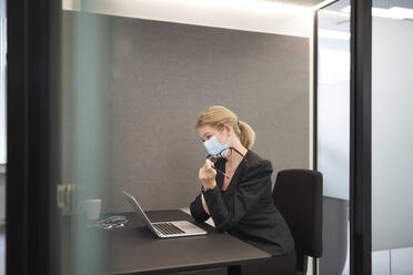 Geschäftsfrau mit Gesichtsmaske arbeitet am Laptop im Büro - JAHF00099