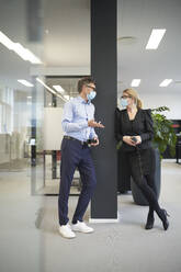 Businessman and businesswoman wearing protective face masks and talking in office - JAHF00102