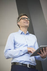 Lächelnder Geschäftsmann mit Tablet-PC träumt im Büro - JAHF00110