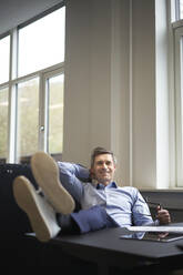 Smiling businessman relaxing in office - JAHF00120