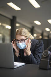 Geschäftsfrau mit Gesichtsschutzmaske bei der Arbeit an einem Laptop am Bürotisch - JAHF00122