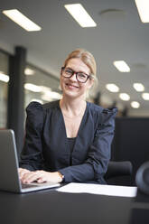 Lächelnde Geschäftsfrau mit Laptop am Bürotisch - JAHF00124