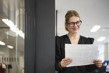Lächelnde Geschäftsfrau bei der Prüfung von Dokumenten im Büro - JAHF00129