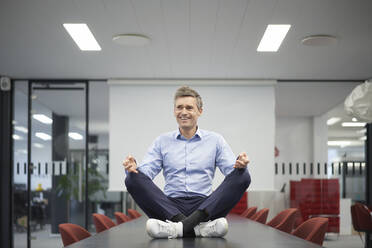 Smiling businessman meditating in meeting room at office - JAHF00146