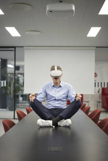 Geschäftsmann mit VR-Brille auf dem Konferenztisch im Besprechungsraum sitzend - JAHF00147