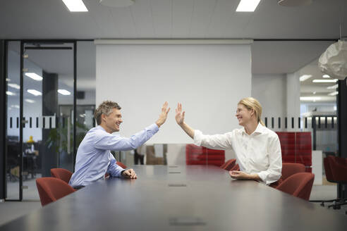 Smiling business colleagues giving high-five in meeting room - JAHF00159