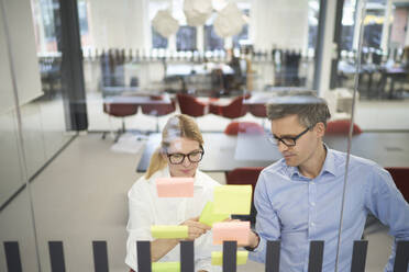 Businesswoman discussing with colleague over adhesive note in meeting room at office - JAHF00168