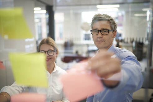 Businessman sticking adhesive note by colleague in board room - JAHF00169