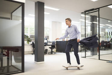 Businessman skateboarding in modern office - JAHF00173
