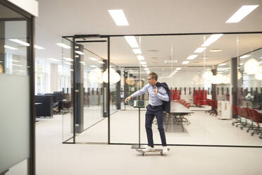 Geschäftsmann fährt Skateboard in einem modernen Büro - JAHF00174