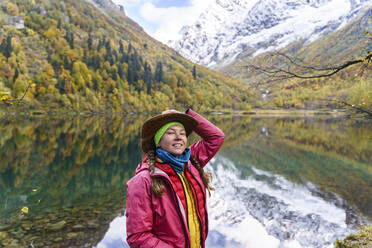 Woman standing in front of mountain reflecting on lake, Caucasus Nature Reserve, Sochi, Russia - OMIF00607