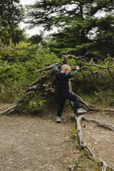 Playful boy climbing fallen tree in forest, Crimea - SEAF00510