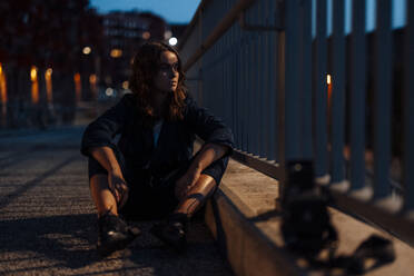 Nachdenkliche junge Frau, die nachts am Geländer sitzt - GUSF06781
