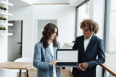 Young businesswoman discussing with businessman over laptop at coworking office - GUSF06782