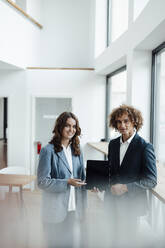 Smiling businessman and businesswoman with tablet PC standing in office - GUSF06785