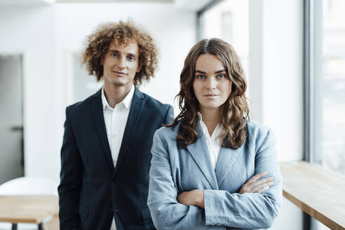 Confident businesswoman with arms crossed standing in front of businessman in office - GUSF06792
