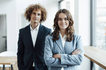 Smiling young businesswoman with arms crossed standing in front of colleague in office - GUSF06793