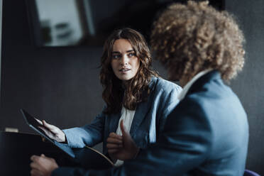 Young businesswoman with tablet PC looking at colleague discussing strategy in office - GUSF06812