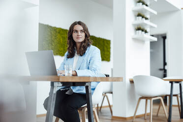 Schöne junge Geschäftsfrau mit Laptop sitzt am Schreibtisch im Büro - GUSF06818