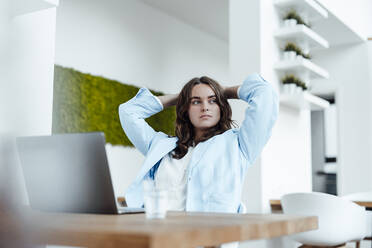 Relaxed businesswoman with hands behind head sitting at desk in office - GUSF06819