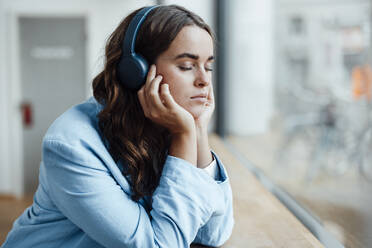 Geschäftsfrau mit geschlossenen Augen hört Musik über drahtlose Kopfhörer im Büro - GUSF06826
