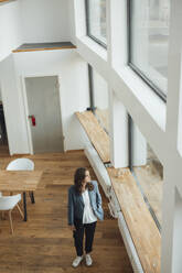 Businesswoman standing with hand in pocket looking through window - GUSF06831