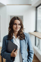 Smiling businesswoman with tablet PC standing in office - GUSF06834