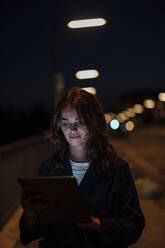 Lächelnde junge Frau, die nachts mit einem Tablet-PC im Internet surft - GUSF06855