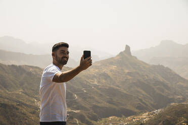 Smiling man taking selfie through mobile phone at Degollada de Becerra, Spain - RSGF00857